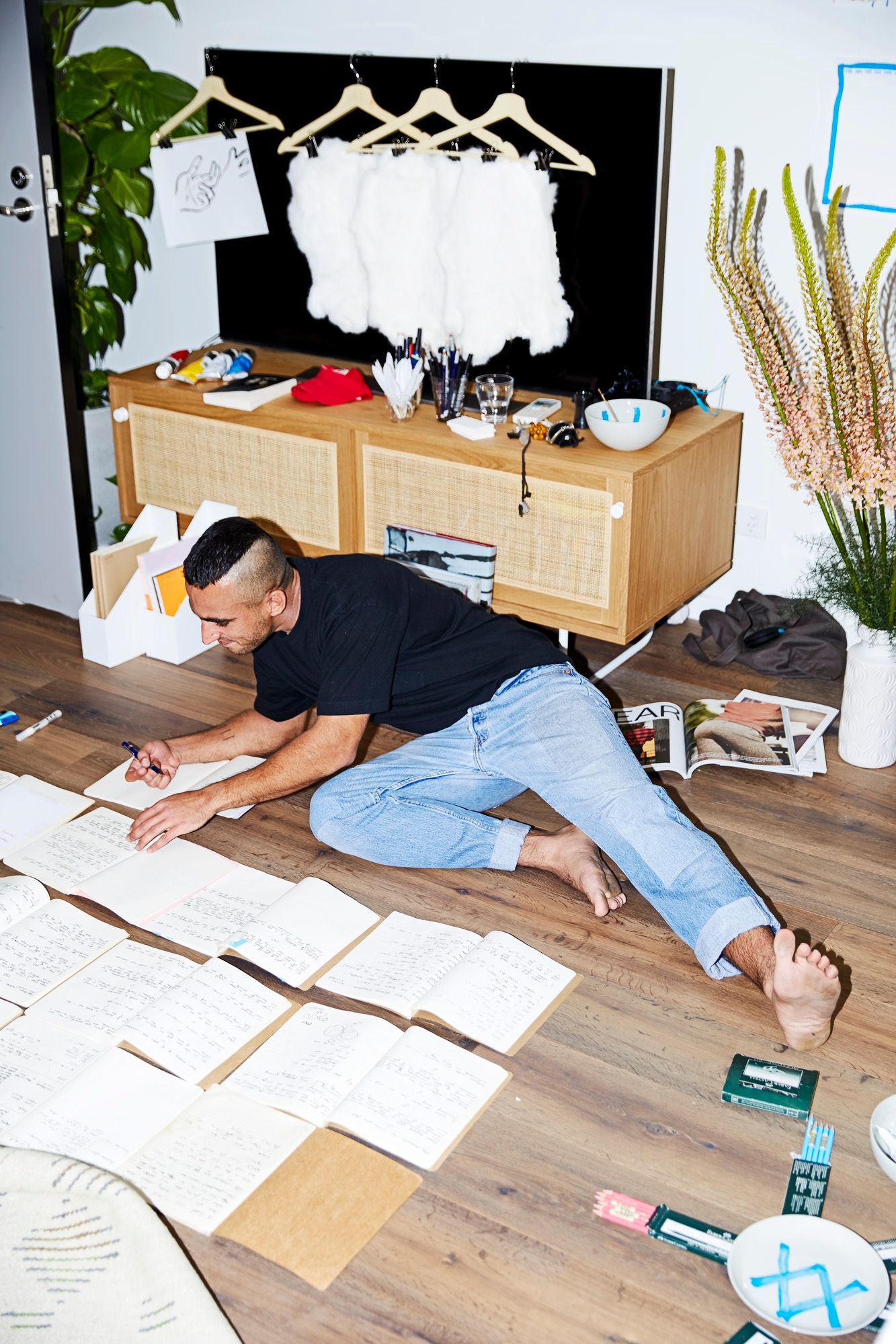 Nabil Sabio Azadi stretched across the studio floor, writing in one of the many notebooks laid out open around him.